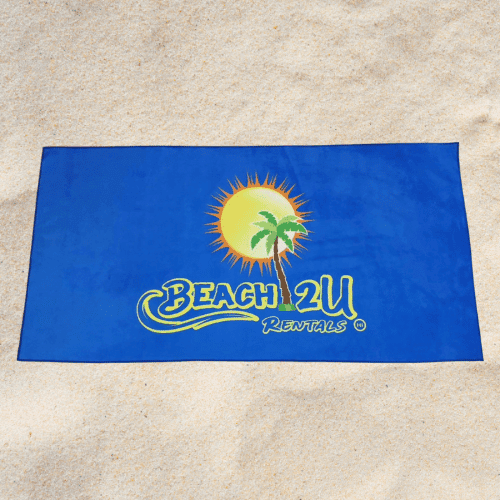 A beach towel from the "Beach 2U Rentals" line shows a blue background with a yellow sun and green palm trees, spread out on sandy ground.