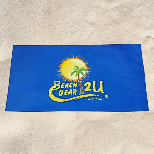 Blue beach towel laid on sand featuring the Beach Gear 2U logo with a sun and palm tree.